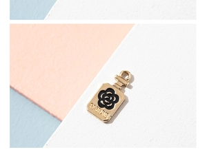 Macro detail of gold-plated perfume bottle charm with black camellia flower oil drop