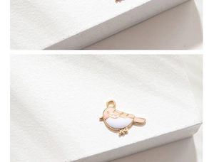 Detailed macro view of a bird charm with pink enamel and gold-plated metal frame