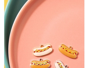 Macro-detail van vier emaille hotdog-bedeltjes op roze schijf voor DIY-sieraden