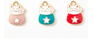 Détail de trois breloques chat porte-bonheur en rose, cyan et rouge avec bord doré