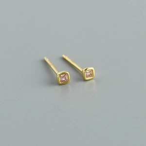 Macro shot of minimalist gold studs featuring square pink zircon stones on grey background