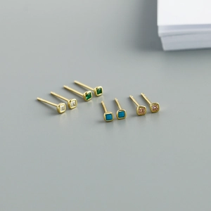 Close-up of four pairs of small square zircon stud earrings in various colors