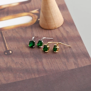 Close-up of gold and silver S925 stud earrings with square green zircon on a display