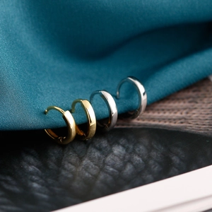 Primer plano de pendientes de aro minimalistas en oro y plata sobre tela azul rugosa