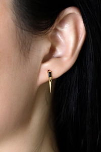 Vue macro de boucles d'oreilles dorées avec zircon noir et pendentif cône minimaliste