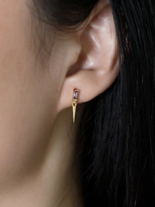 Gros plan sur boucle d'oreille dorée avec pierre de zircon violet et pendentif conique