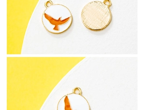 Detail of round bird pendant with white enamel front and golden brushed metal back