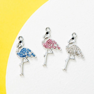 Three rhinestone flamingo pendants in pink, blue and white on a mustard yellow background