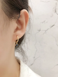 Détail d'une boucle d'oreille huggie en or avec pierre bleu saphir sur l'oreille