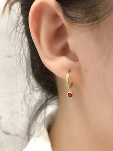 Détail de boucles d'oreilles dorées avec pierre rouge et micro-incrustations scintillantes