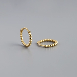 Close-up of golden beaded hoop earrings with vintage texture on a grey background