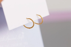 Primer plano de aretes de aro en oro de 18K con diseño de cuerda trenzada elegante