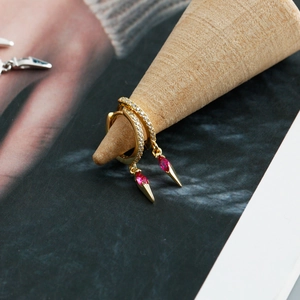 Detailed shot of gold hoop earrings with red marquise stone and zircon on wooden stand