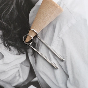 Detail van zilveren druppeloorbellen aan een houten kegel bij een modetijdschrift