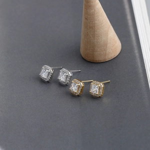 Detailed view of silver and gold square halo earrings with zircon studs on grey surface