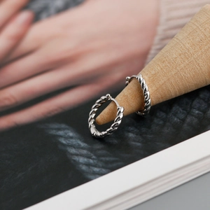 Macro view of twisted rope texture on silver hoop earrings displayed on a wooden stand