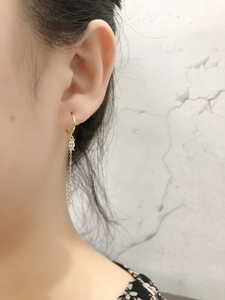 Dettaglio dell'orecchino pendente dorato con zirconi quadrati indossato da una modella