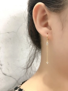 Dettaglio dell'orecchino a nappine dorato con zircone su modella e sfondo marmo