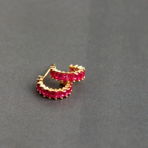 Detail of gold earrings with rectangular rose red zircons in a semi-circle design