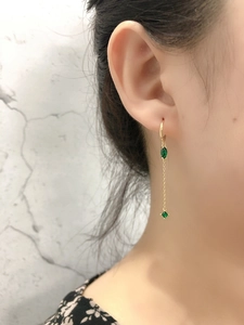 Dettaglio di orecchini a nappa dorata con zirconi verde oliva indossati da una modella