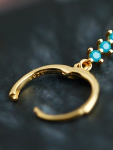 Vue macro du poinçon S925 sur des créoles dorées avec pierres de zircone bleu turquoise