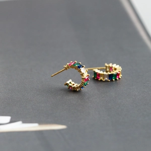 Macro shot of C-shaped gold earrings with rectangular multi-color cubic zirconia settings