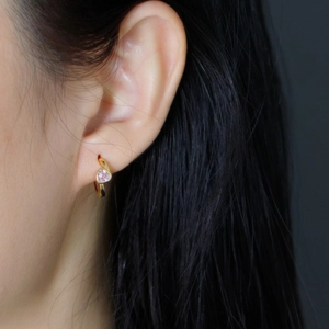 Gros plan de boucles d'oreilles cœur dorées avec pierres roses sur une oreille