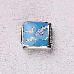 Détail macro du charm italien en émail bleu avec motif oiseau blanc sur acier inoxydable