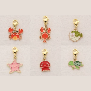 Set of 6 colorful enamel ocean creature charms with gold lobster clasps on beige background