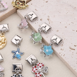 Detail of Italian charms with enamel flowers and starfish on a beige stone surface