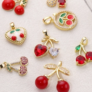 Golden cherry pendants with red crystals and green enamel on off-white fabric texture