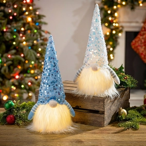 Macro shot of two glowing Christmas gnomes with LED lights and sequined hats on wood