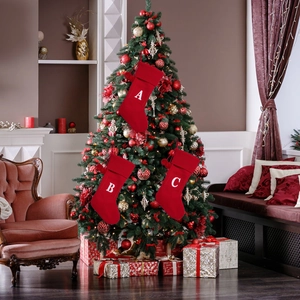 Detail of red knitted Christmas stockings with letters A, B, and C hanging on a festive tree