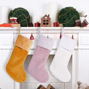 Three plush Christmas stockings in gold, pink, and white hanging on a cozy fireplace mantel