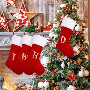 Red velvet Christmas stockings with gold glitter letters and white plush trim hanging on a fireplace