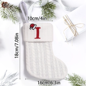 Detail of white cable knit Christmas stocking featuring red embroidered letter I and mini hat