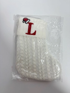 Close-up of white knit Christmas stocking with red embroidered letter L and mini hat