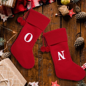 Pair of red knitted Christmas stockings with white letters O and N on a rustic wood background