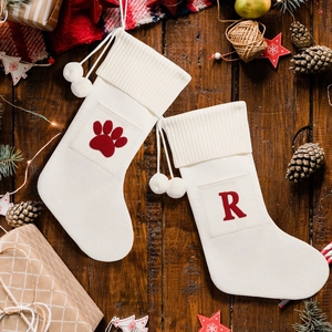 Detail of cream cable knit Christmas stockings with red letter R and paw prints on wood
