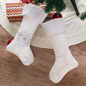 Pair of white faux fur Christmas stockings with silver sequin snowflakes on wood floor