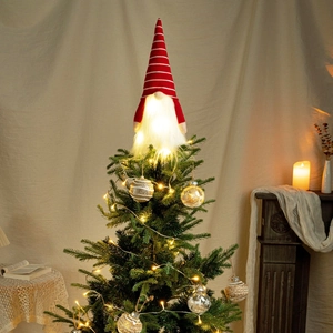 Macro view of glowing LED Christmas gnome tree topper with red striped knitted hat