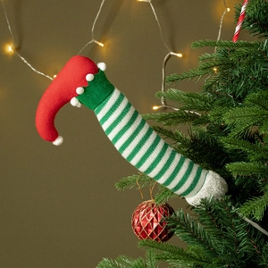 Detailed view of striped Christmas elf legs with red boots nestled in pine tree branches