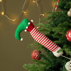Detailed view of striped Christmas elf leg hanging on a festive tree with warm LED lights