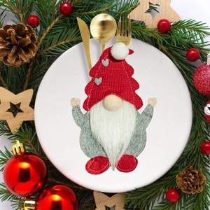 Detail of Christmas gnome cutlery holder with red knit hat on a festive dinner plate