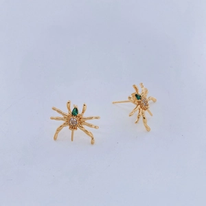 Detalle de pendientes de araña bañados en oro con gemas verdes y cristales blancos