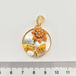 Dettaglio del ciondolo a fiore con smalto arancione e perla naturale accanto a un righello