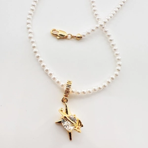 Collier de perles avec pendentif étoile dorée et zircon sur un fond blanc épuré