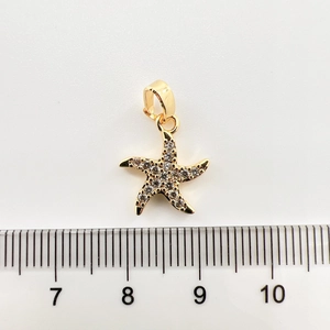 Détail d'un pendentif étoile de mer plaqué or de 1,5 cm avec zircons blancs et règle