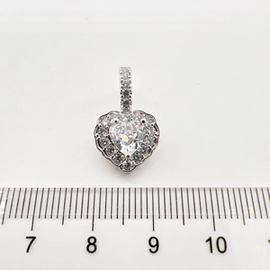 Macro detail of silver heart pendant with cubic zirconia inlay against a measuring scale