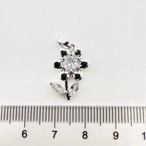 Détail d'un pendentif floral avec zircons blancs et finition argentée à côté d'une règle